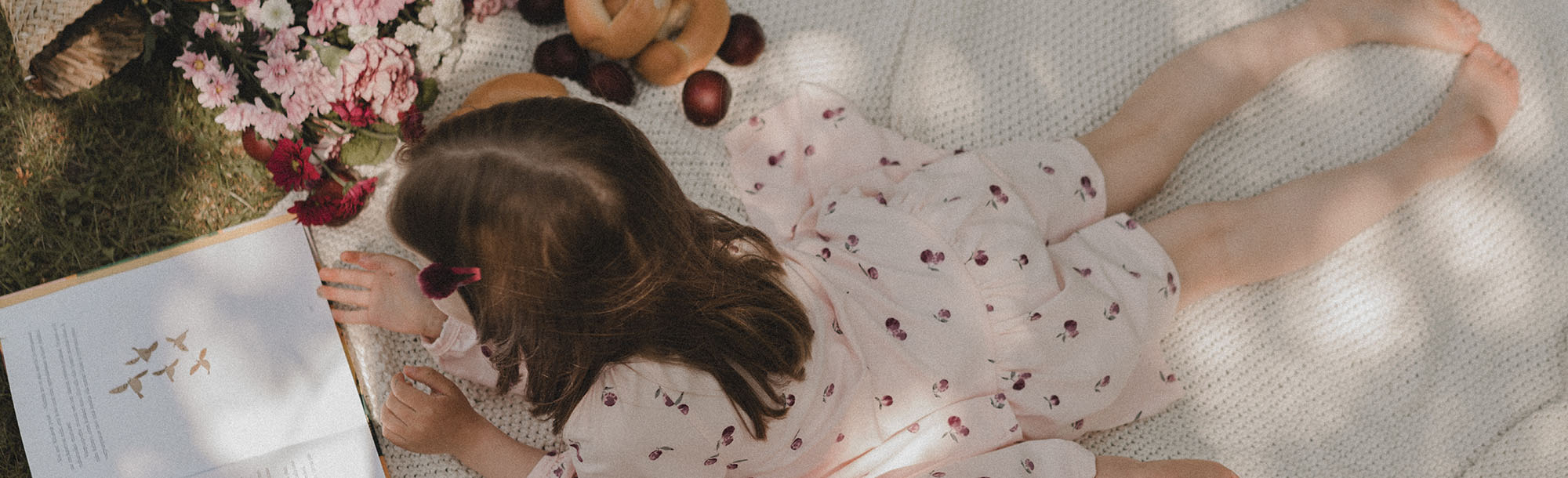 Tyttö kantaa kukkia olalla ja hänellä päällään syreenit-kuosin kesämekko